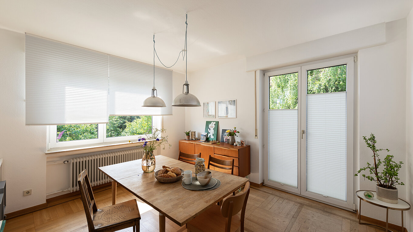 Salle à manger lumineuse avec plissés blancs aux fenêtres et à la porte-fenêtre